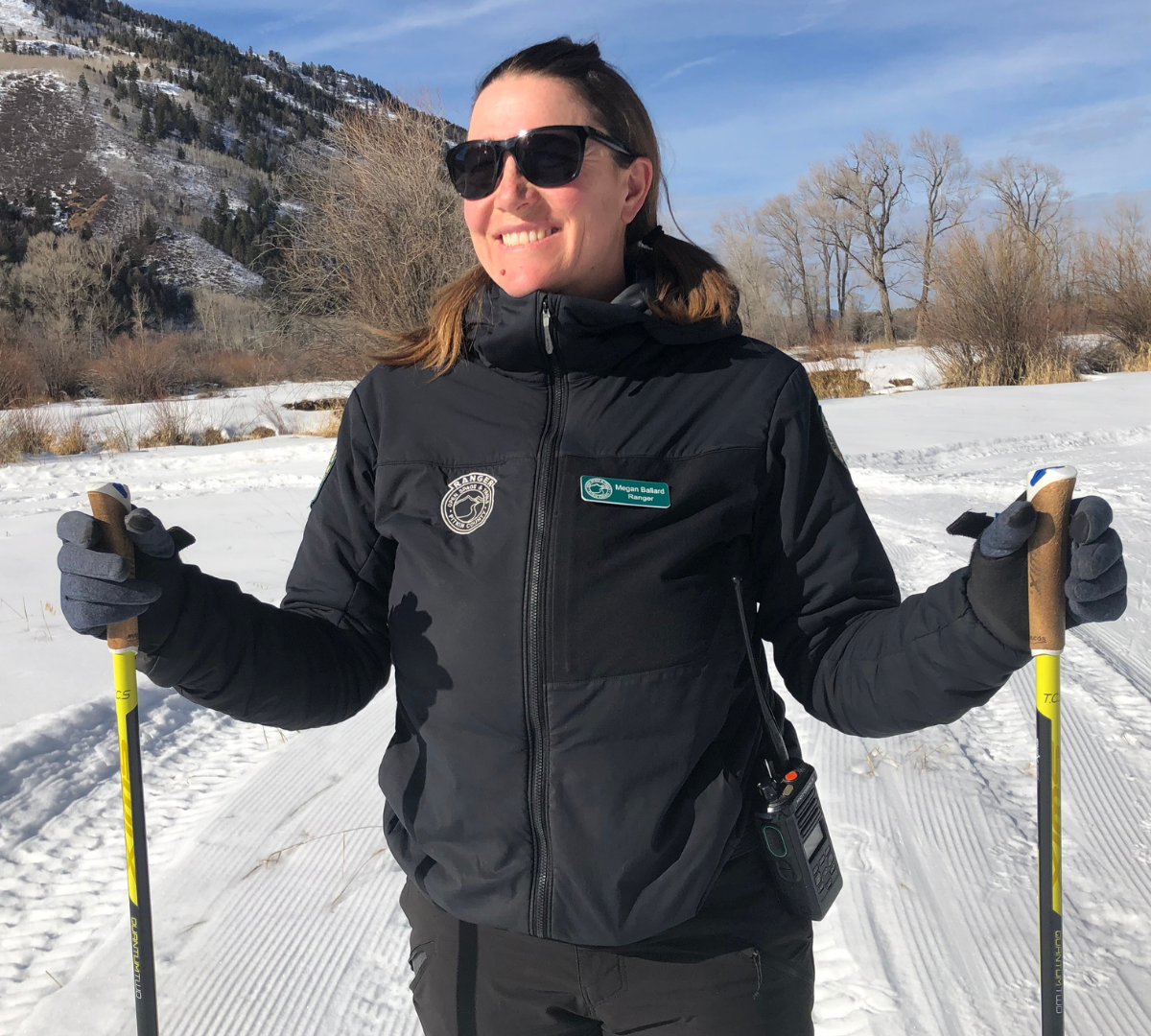 Dark haired female holds ski poles and smiles 