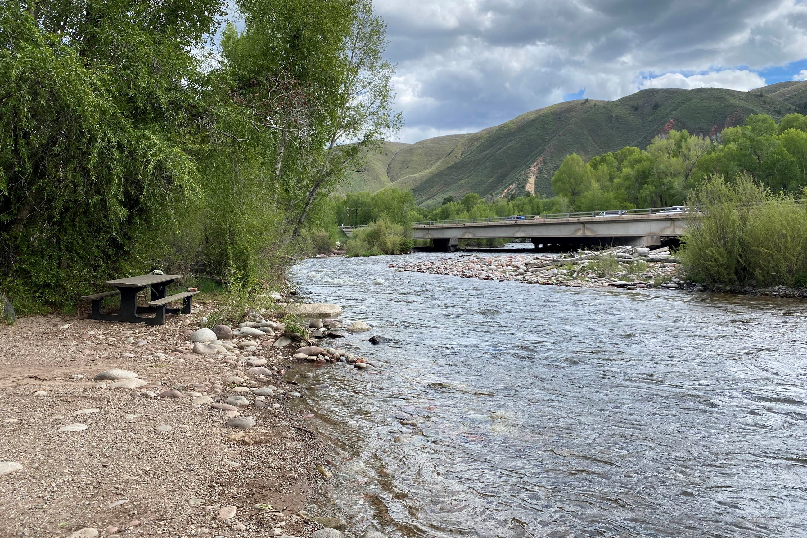 A vacant picnic table along the Roaring Fork River with Highway 82 in the distance.